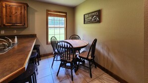 Una cocina con una mesa de comedor, sillas, armarios de madera, una ventana y un letrero en la pared.