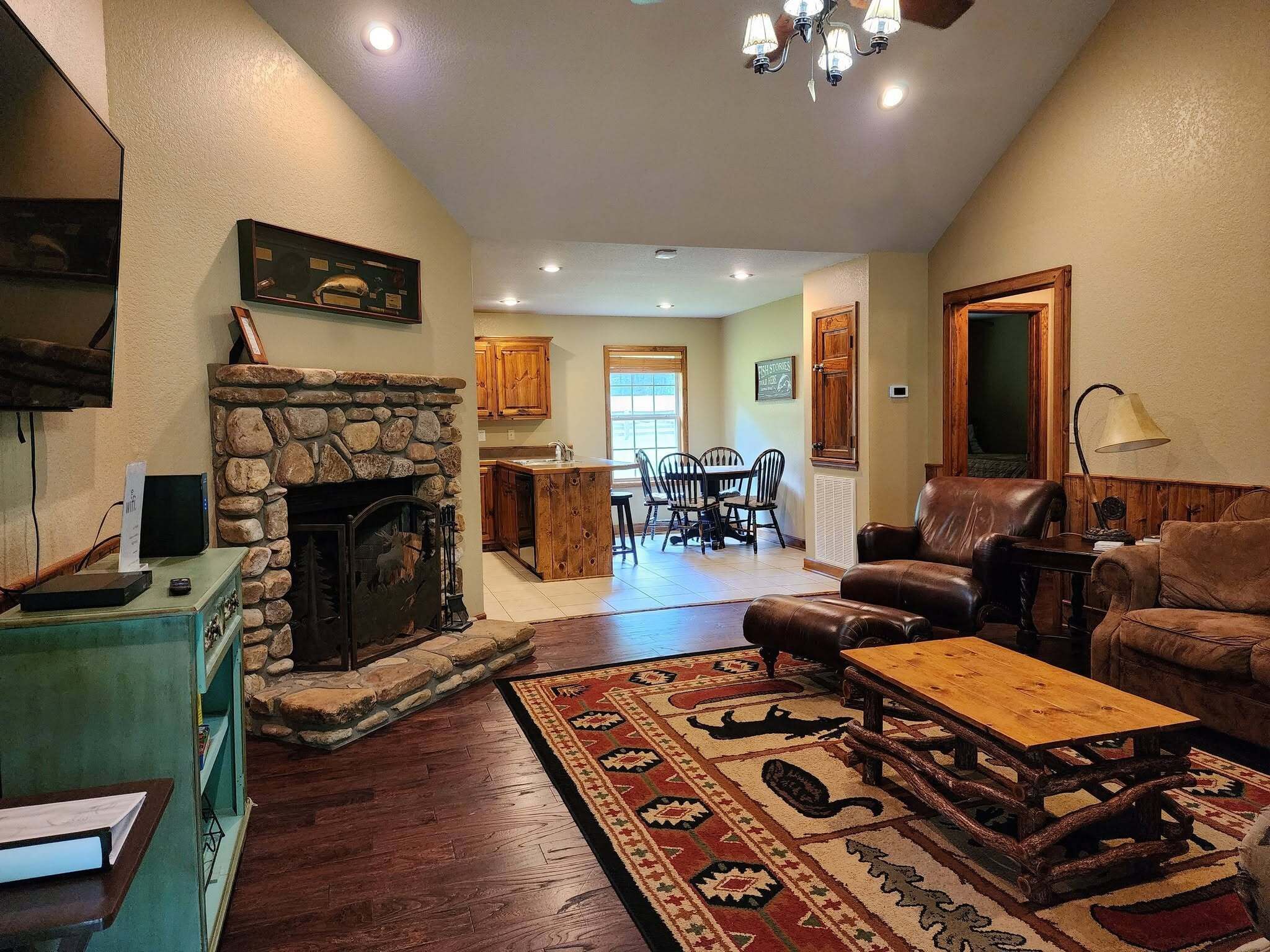 A spacious living room with a stone fireplace, leather furniture, and a dining area in the background.