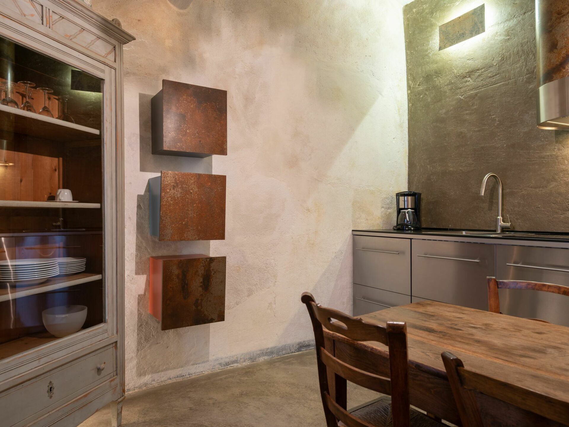 A kitchen with a wooden table, chairs, a coffee maker, and a sink.