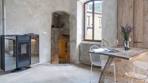 Un interior rústico con pared de piedra, puerta de madera, ventana con vistas, mesa con sillas y un electrodoméstico negro.