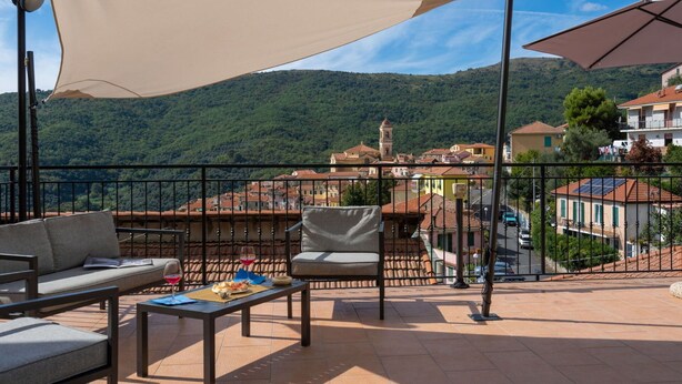 Una terrazza con posti a sedere all'aperto, un tavolo imbandito e vista su una cittadina collinare.