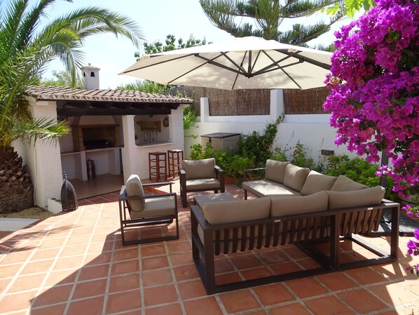 An outdoor patio with a dining area, a sofa, and a pergola with a large umbrella.