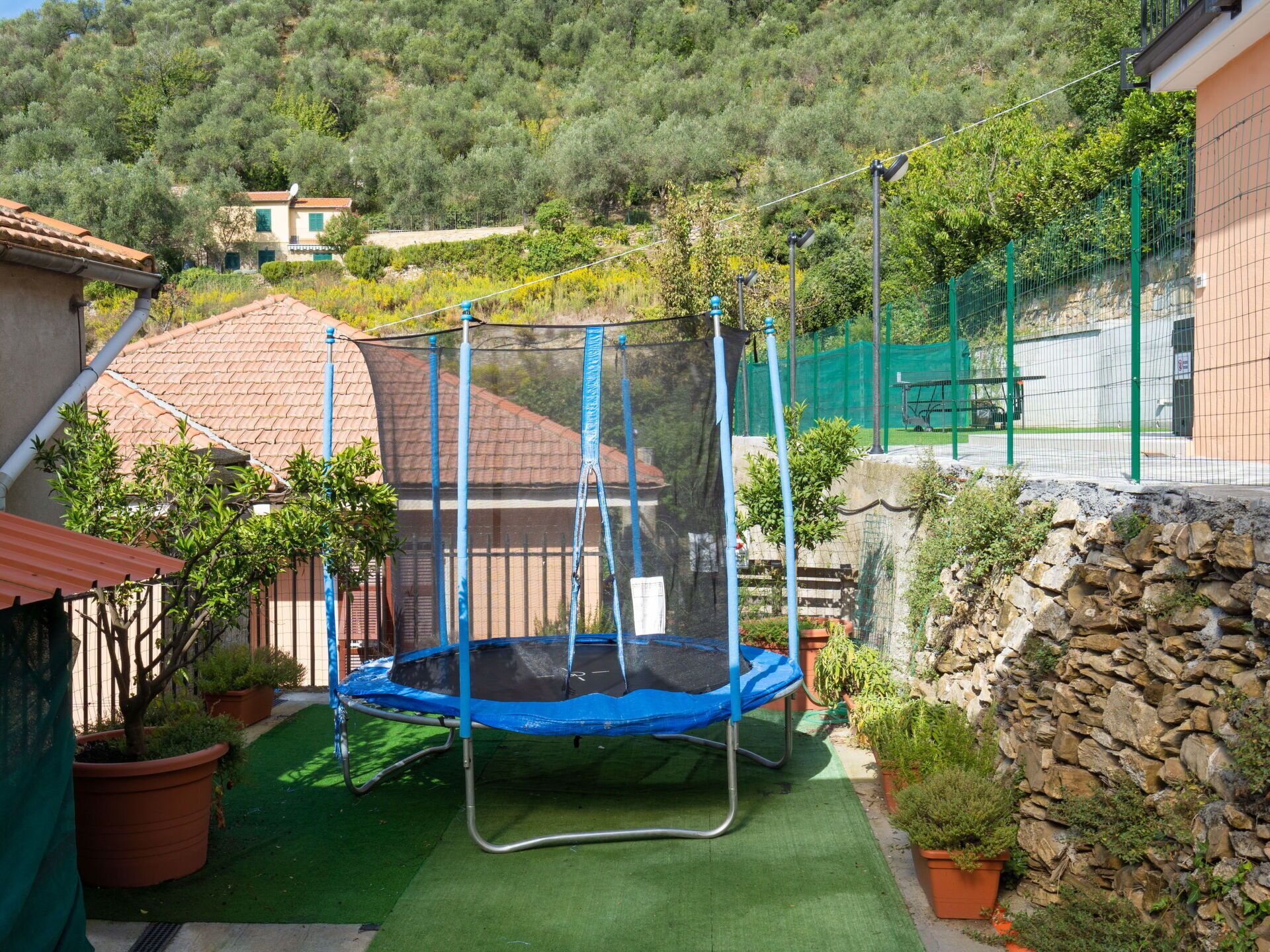 A residential area with a trampoline in a backyard, surrounded by potted plants and a stone wall.