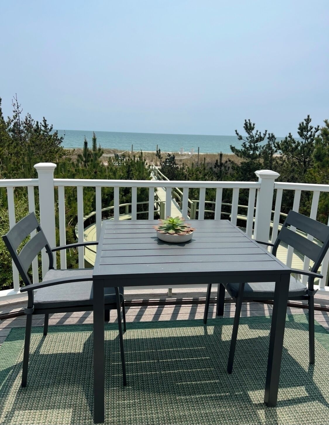 A deck with a table and chairs, overlooking a beach and ocean.