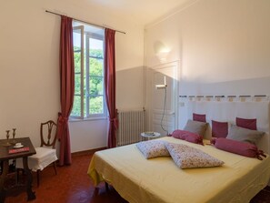 Een slaapkamer met een bed, een stoel, een tafel en een raam met gordijnen.