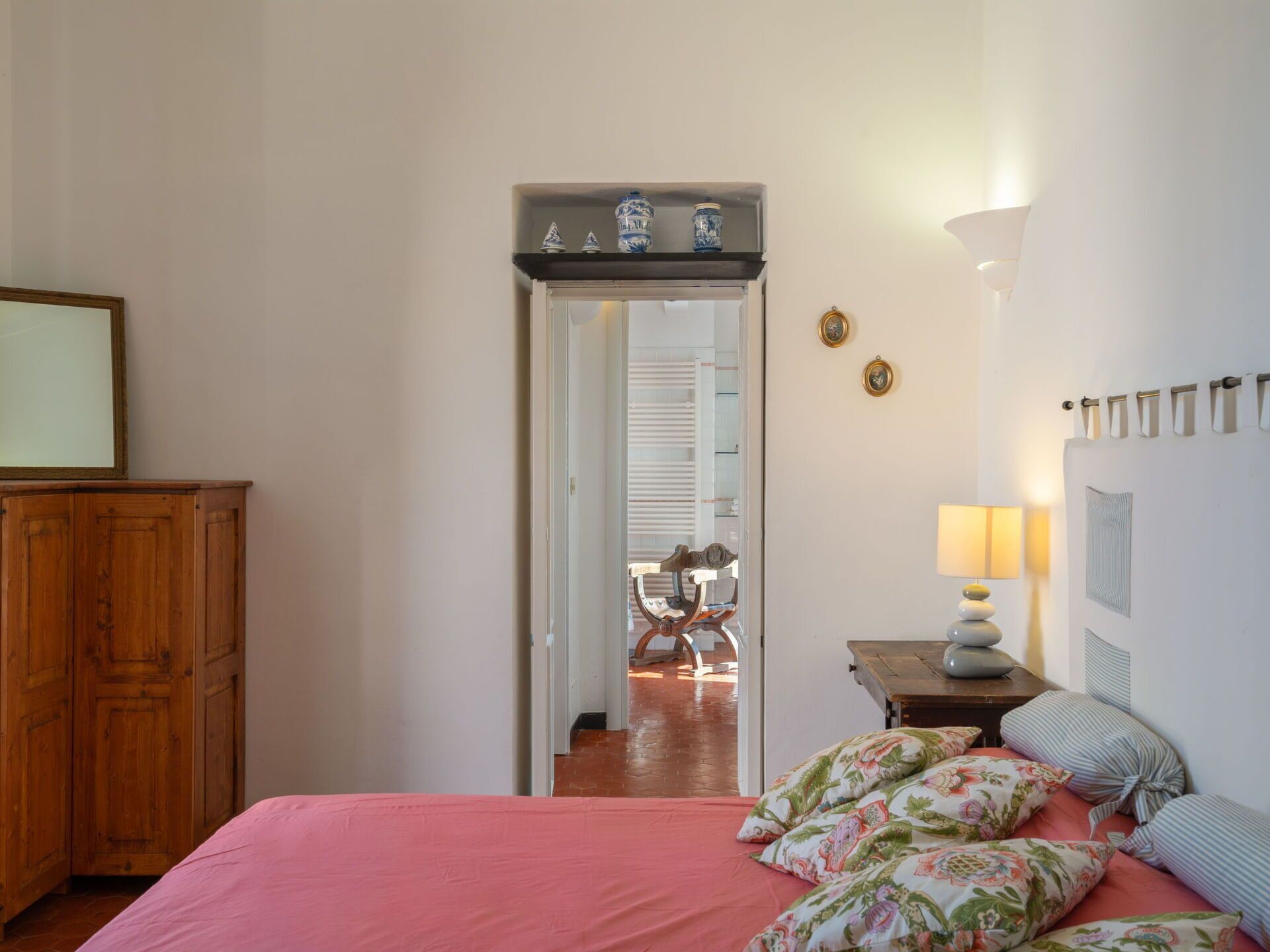 Ein Schlafzimmer mit einem Bett, einem Holzschrank, einem Nachttisch mit Lampe und einer Tür zu einem anderen Raum.