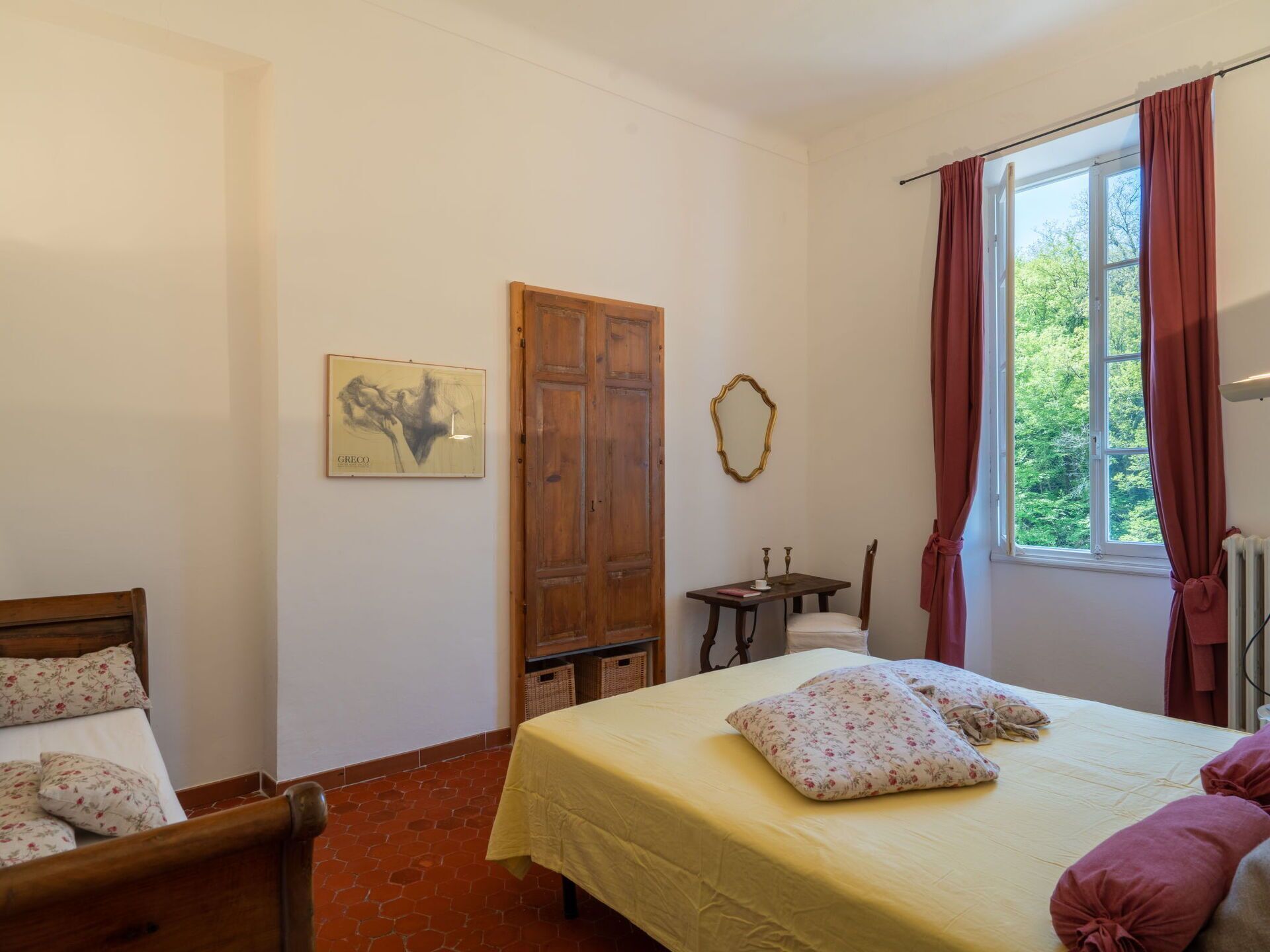 Une chambre à coucher avec un lit, une armoire en bois, une petite table avec une chaise et une fenêtre avec des rideaux.