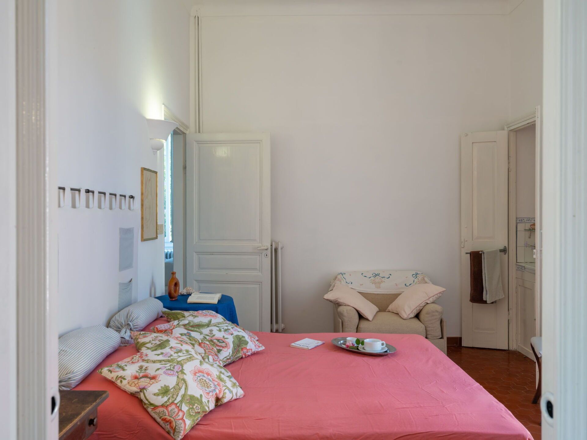 A bedroom with a bed, a chair, a small table, and a door.