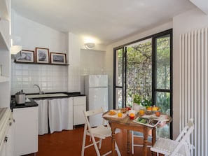 Una cocina con armarios blancos, encimera negra y una mesa de comedor preparada para el desayuno.