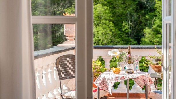 Un balcone con tavolo apparecchiato per mangiare, una sedia e vista su vegetazione rigogliosa.