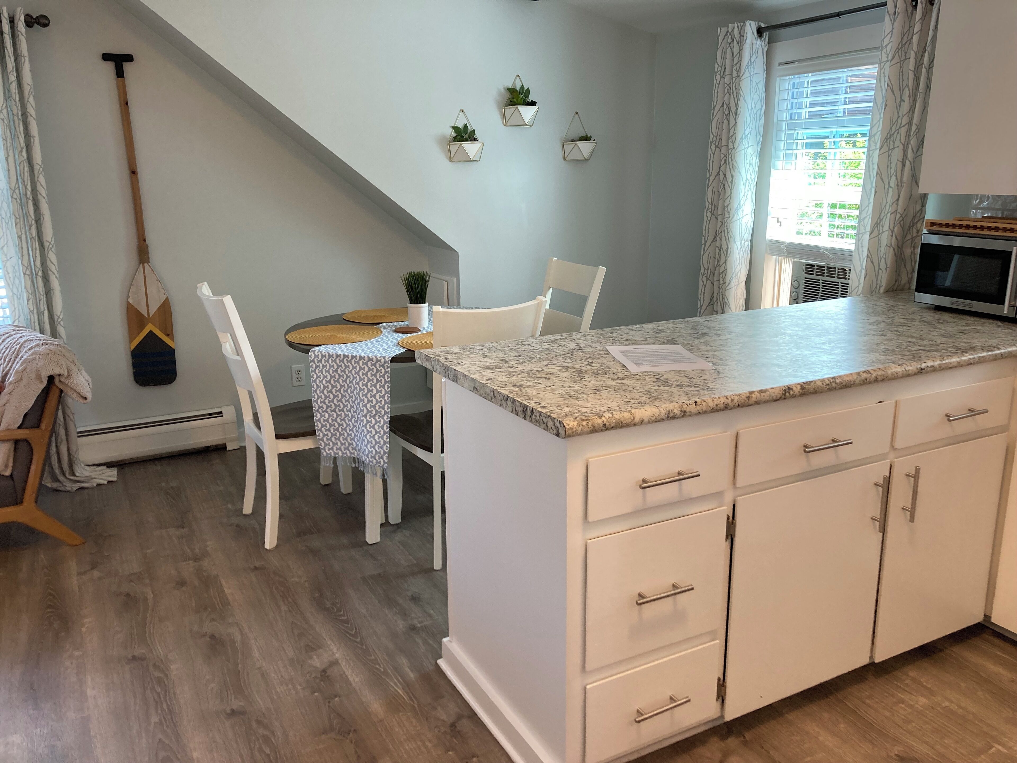 A kitchen with a granite countertop, white cabinetry, a dining area with a table and chairs, and a hanging plant.