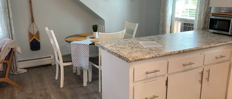 A kitchen with a granite countertop, white cabinetry, a dining area with a table and chairs, and a hanging plant.