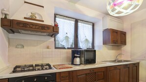 A kitchen with a gas stove, oven, microwave, coffee maker, and a window with curtains. - Cosy apartment for 6 guests with A/C, WIFI, TV, terrace and pets allowed (Castellaro)