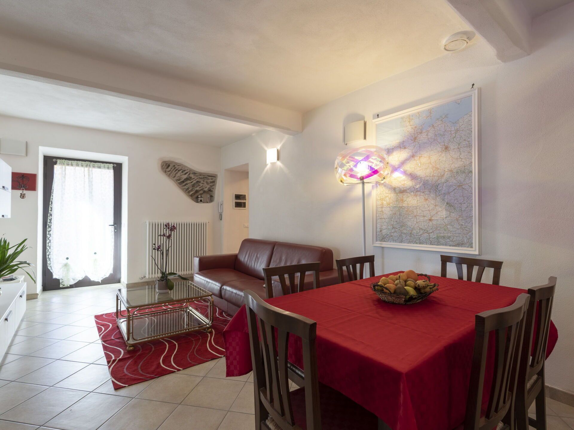 Un coin repas avec une nappe rouge, un saladier de fruits et une carte accrochée au mur.