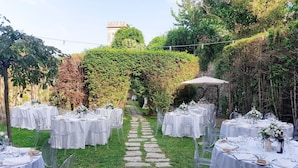 Un lieu de réception en plein air, idéal pour un mariage, avec de nombreuses tables rondes recouvertes de nappes blanches, des chaises transparentes et un chemin de pierre menant à un belvédère.