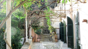 A covered outdoor seating area with metal tables and chairs, surrounded by greenery and a stone wall. - Lovely apartment for 8 guests with WIFI, TV, patio and pets allowed (Finale Ligure)