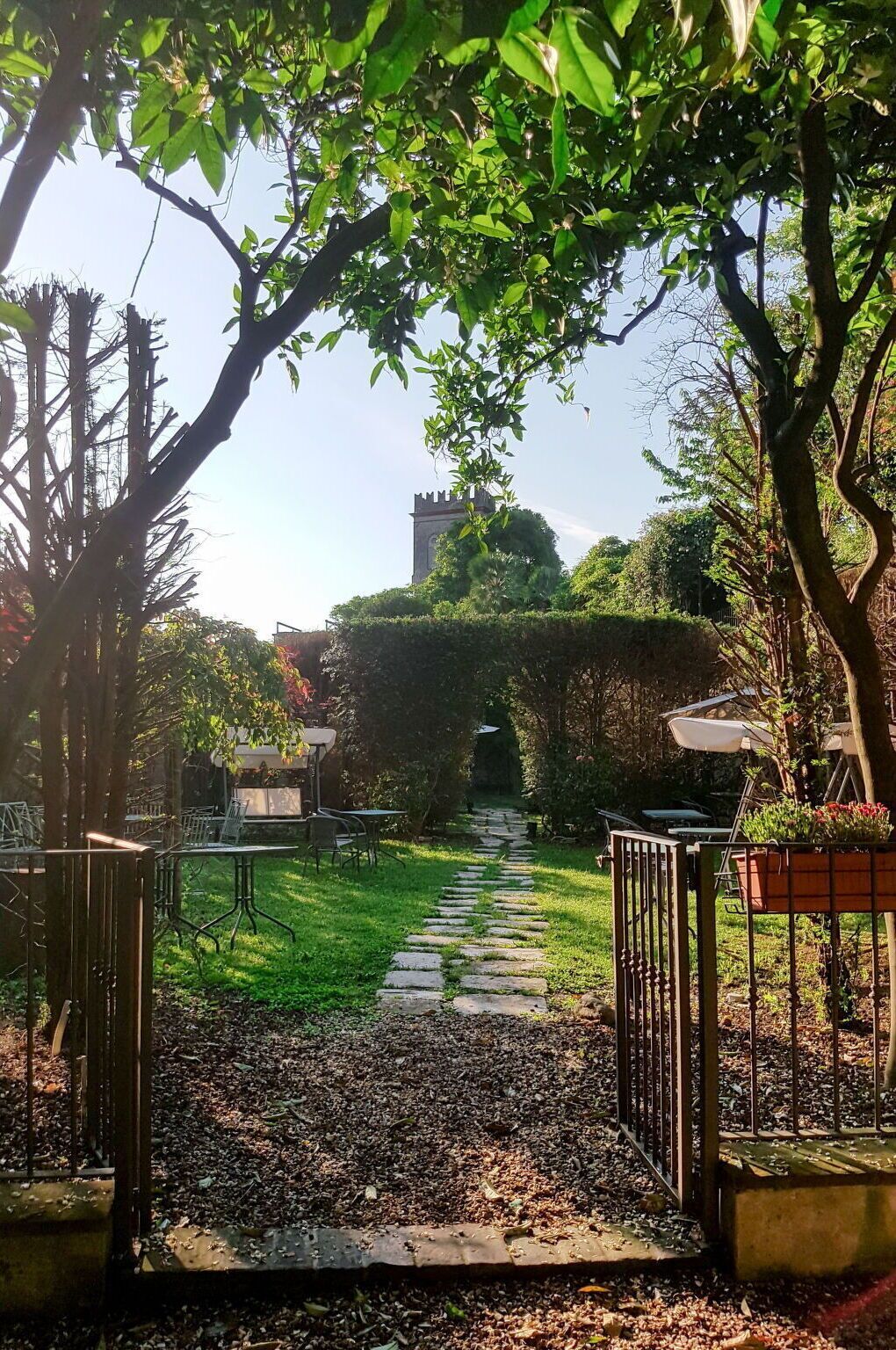 Ein Gartenweg führt zu einem Gebäude mit einem Turm, umgeben von Bäumen und Grünpflanzen.