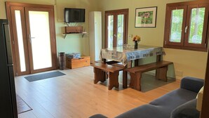 A spacious living room with a wooden floor, a dining table with benches, a sofa, and a television mounted on the wall. - Wonderful private villa for 4 guests with WIFI, TV, terrace and pets allowed (Trarego)