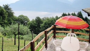 Eine Terrasse mit Tisch und Stühlen, einem Holzgeländer und Blick auf Berge und einen See.