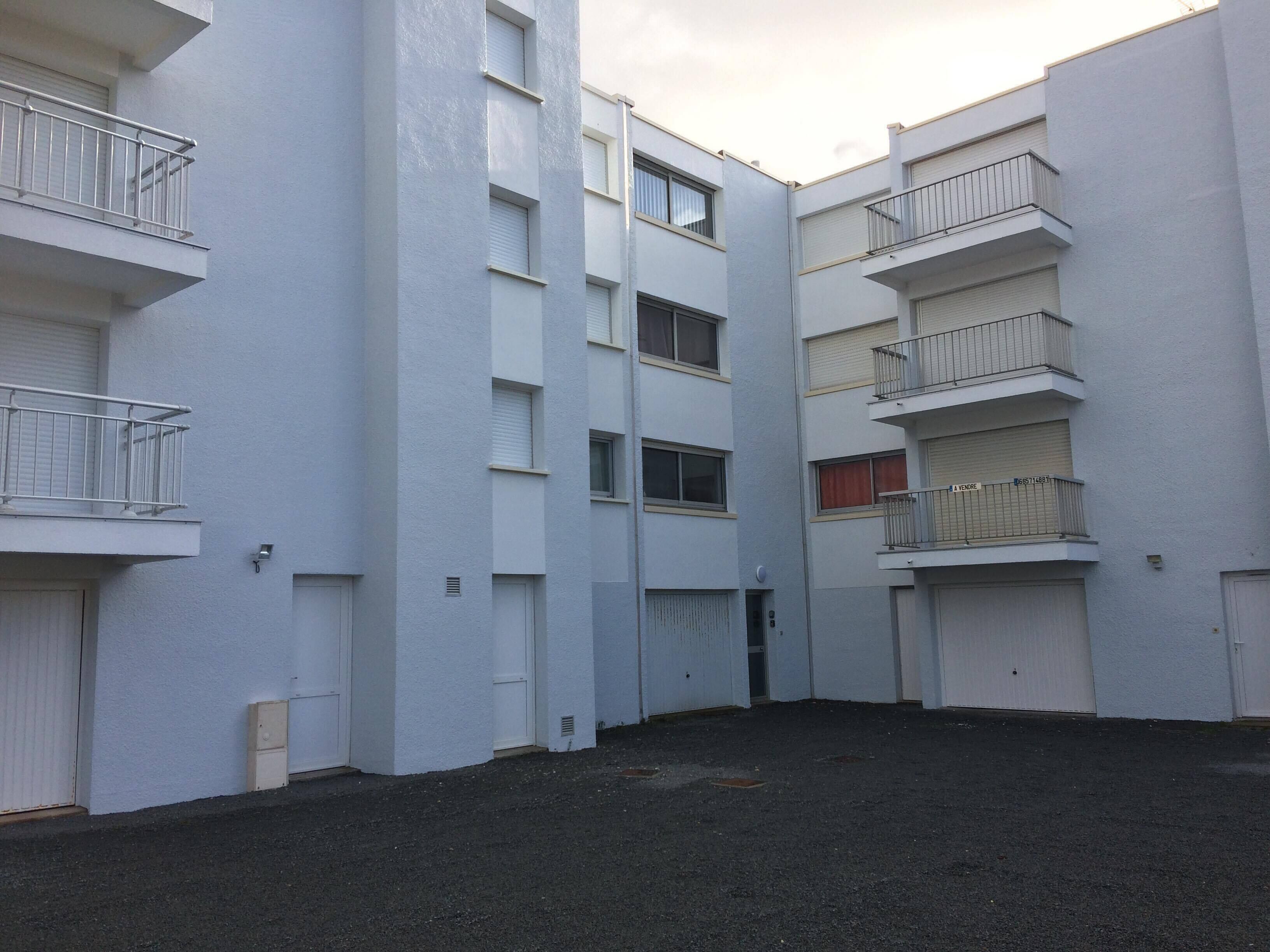 Un immeuble à plusieurs étages doté de balcons, d’une entrée sécurisée et d’une zone au sol dallée.