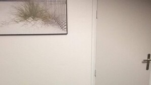A small room with a grey sofa, a green throw blanket, and a door. - Studio Casa Marina in Sainte Cécile Plage (Sainte-Cécile Plage)