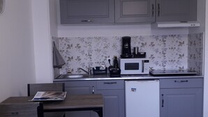 A compact kitchen with grey cabinets, a white refrigerator, a microwave, and a small sink. - Studio Casa Marina in Sainte Cécile Plage (Sainte-Cécile Plage)