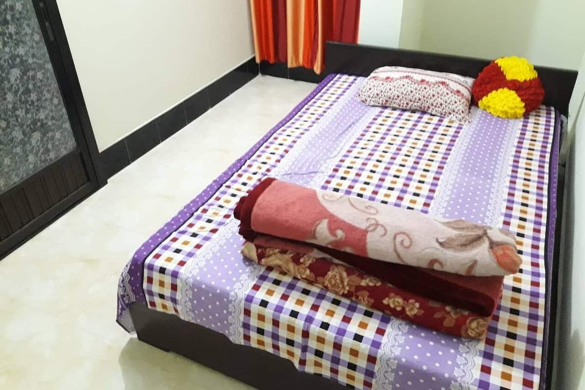 Una cama bien hecha con colcha de cuadros, almohadas y un plaid enrollado, además de un cojín decorativo en la cabecera.