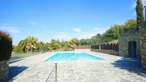 Una piscina rectangular con un borde de piedra, rodeada por una valla de madera y muros de piedra, con árboles y un cielo despejado al fondo.