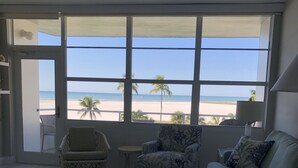 Un salon spacieux doté d’une grande fenêtre donnant sur une plage, et aménagé avec un canapé, des fauteuils et une table basse.