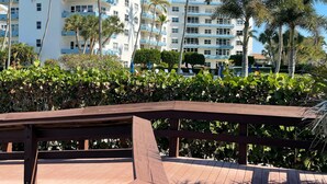 Une terrasse en bois offrant une vue sur un hôtel à plusieurs étages, doté de balcons et bordé de palmiers.