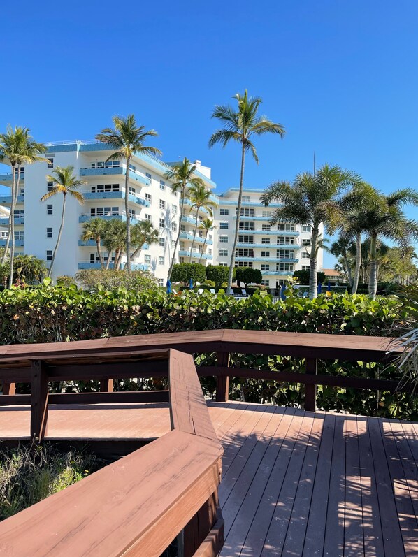 Um deck de madeira com vista para um hotel de vários andares, com varandas e palmeiras.