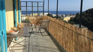 Un balcon avec vue sur la mer, des meubles en osier et une clôture en bambou.