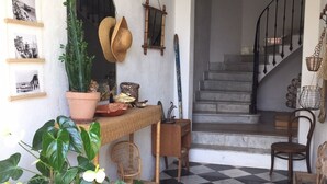 Un sol à carreaux, un escalier, des meubles en osier et une plante en pot.