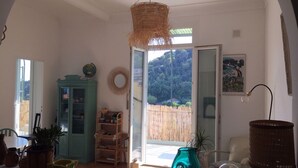 Une pièce lumineuse avec une grande fenêtre, un lustre en osier et un vase de couleur turquoise.