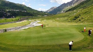 Ein Golfplatz mit Bergkulisse, einer Steinmauer und einem Bach.