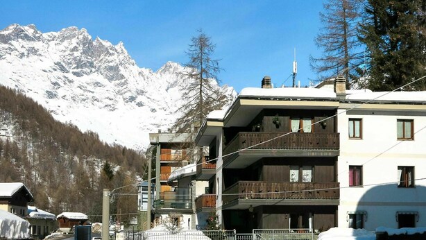 Un immeuble à plusieurs étages doté de balcons, avec une chaîne de montagnes en arrière-plan et un paysage enneigé.