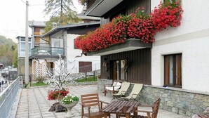 Un espace patio doté d’un sol en pierre, de meubles en bois et de jardinières ornées de fleurs rouges.