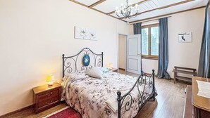Un dormitori amb llit, una tauleta de nit, una làmpada penjant, una finestra amb cortines i una porta.