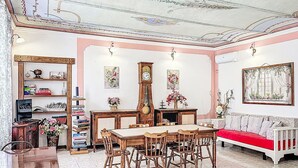 Zona de menjador amb una taula i cadires de fusta, un rellotge i un sofà amb un coixí vermell.
