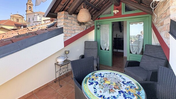 Een balkon met rieten meubilair, een betegelde vloer en uitzicht op gebouwen op de achtergrond.