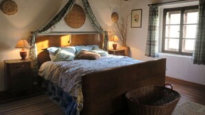 Ein gemütliches Schlafzimmer mit einem hölzernen Bett, zwei Nachttischen mit Lampen, einem Korbwäscheschrank und einem Fenster mit Vorhängen.