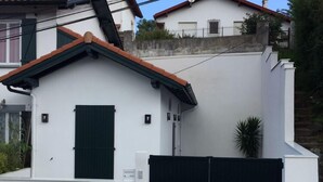 Ein weißes Gebäude mit grünem Fensterladen, einem schwarzen Tor und einem kleinen Topfpflanzen.