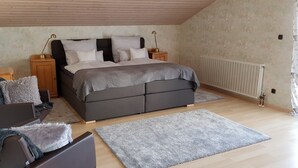 A bedroom with a bed, nightstands, a wooden bench, and a radiator. - Großzügige Ferienwohnung in der Schlössergemeinde Küps (Küps - Tüschnitz)