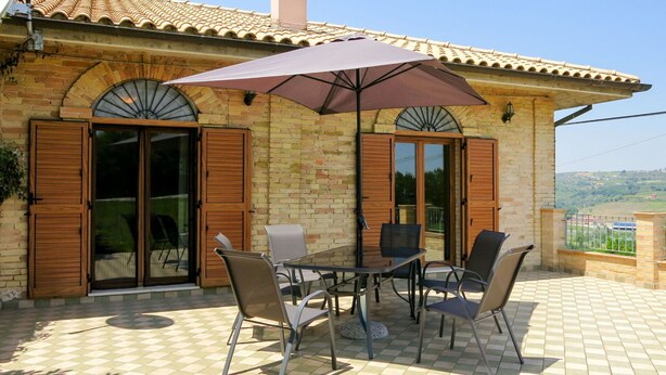 A patio with a table and chairs, a large umbrella, and a brick building with wooden shutters and a chimney. - Beautiful private villa for 4 people with WIFI, TV, terrace and pets allowed (Picciano)