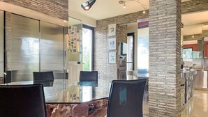 Een moderne eetruimte met een glazen tafel, zwarte stoelen en een accentmuur van natuursteen.