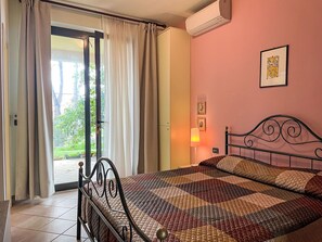 Une chambre à coucher avec un lit, des rideaux, un appareil de climatisation et une vue sur la verdure à l’extérieur.