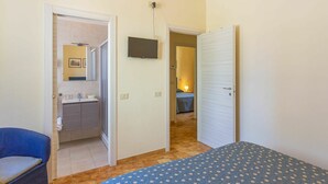 Un dormitorio con cama, una silla, un televisor y un baño con lavabo y espejo.