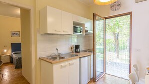A compact kitchen with white cabinets, a microwave, and a sink. There is a dining area with a table and chairs, and a sliding glass door leading to an outdoor area.