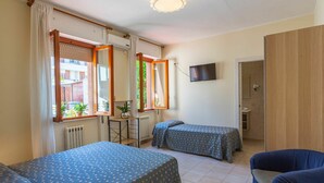 A room with two beds, a small table, a TV, and a bathroom door.