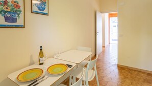 A dining area with a table set for two, a bottle of wine, and two plates with a colorful design. There are framed botanical prints on the wall and a hallway leading to another room.